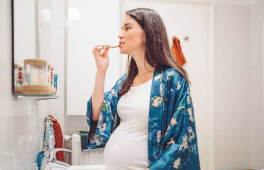 Pregnant woman brushing her teeth at home to maintain healthy gums and protect her baby during pregnancy