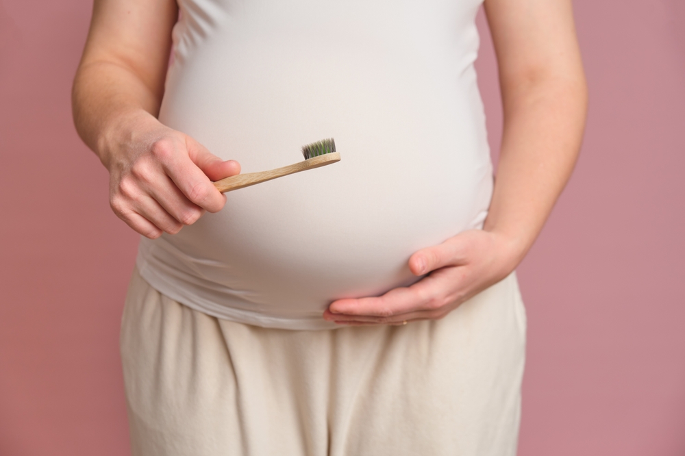 Pregnant woman holding a toothbrush, studio pink background. Concept of pregnancy and brushing teeth