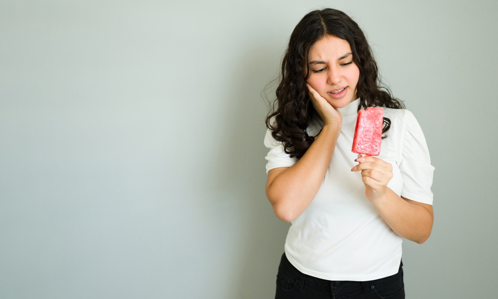 Young woman experiencing tooth sensitivity while eating a popsicle, suffering from dentin hypersensitivity