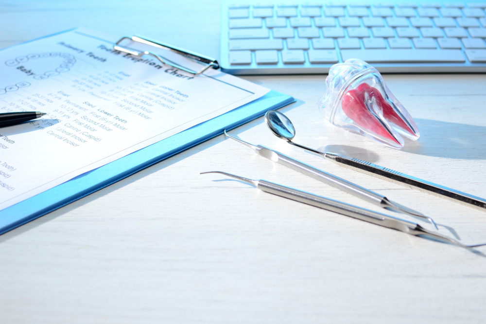 Dentist tools, tooth eruption chart and tooth meridian chart, model on dentist table with computer keyboard. Dental probe, mirror and explorer, with copy space. Dental hygiene and healthcare concept.