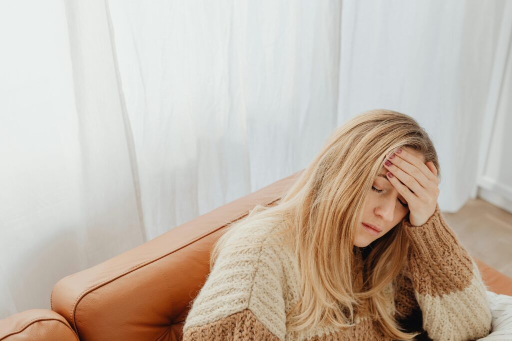 A woman in a knitted sweater sits with a headache on a cozy sofa indoors. Can a Tooth Infection Cause Headaches