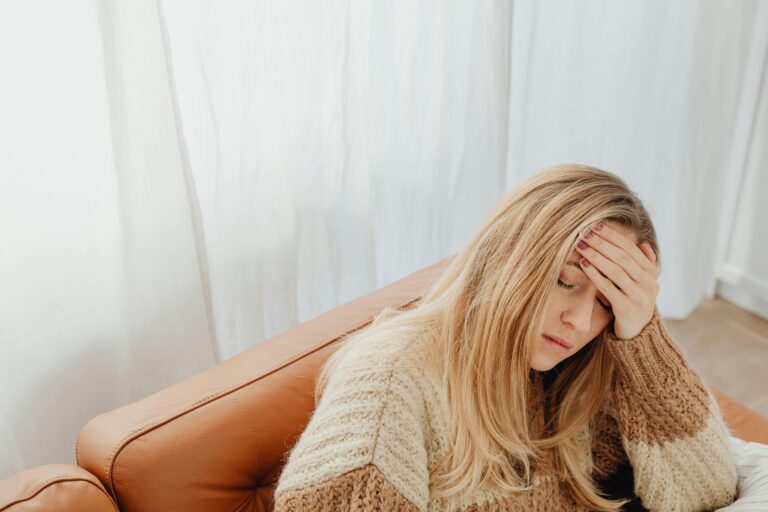 A woman in a knitted sweater sits with a headache on a cozy sofa indoors. Can a Tooth Infection Cause Headaches